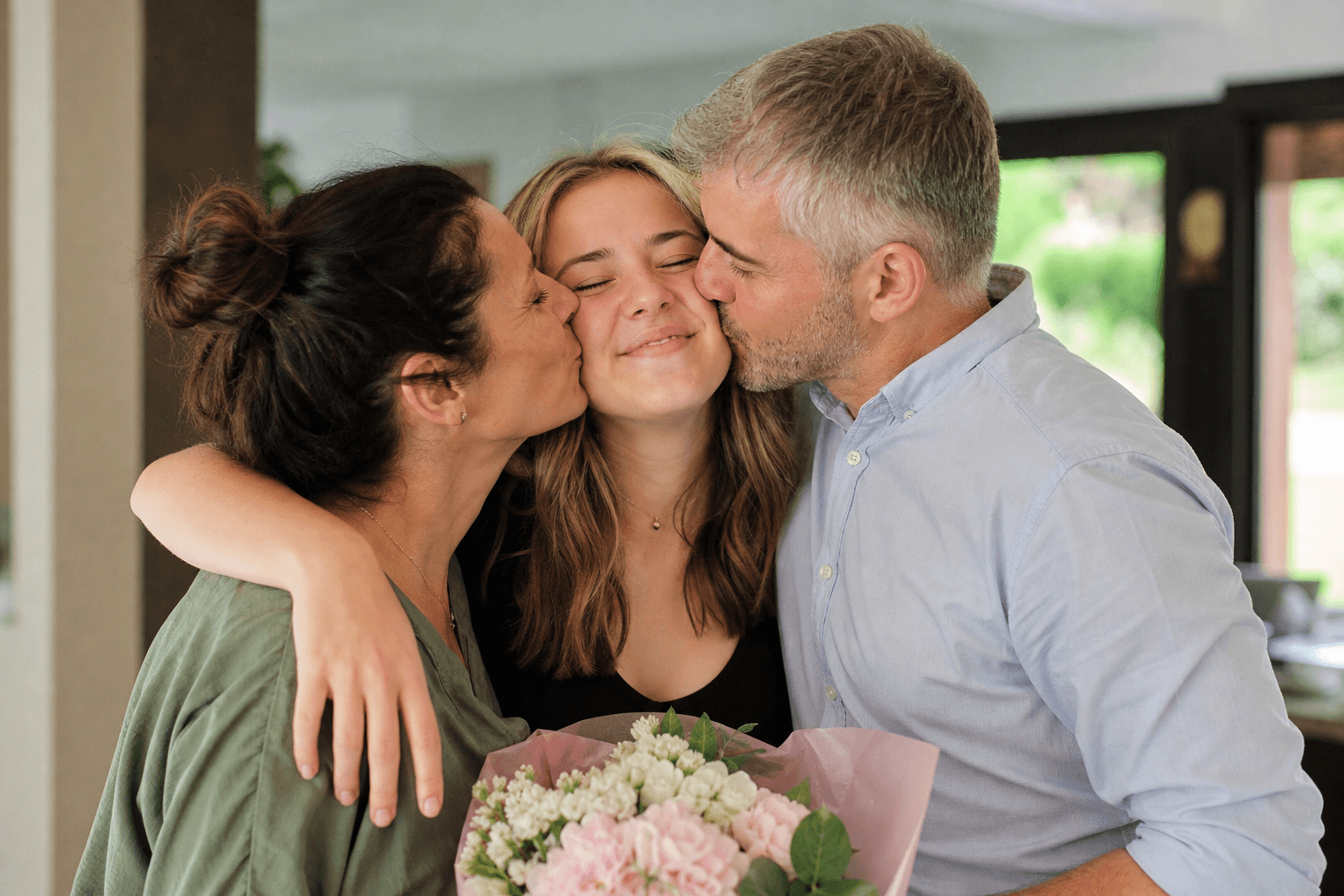 Eltern umarmen ihr Kind nach dem bestandenen Abitur und wirken stolz und gerührt.