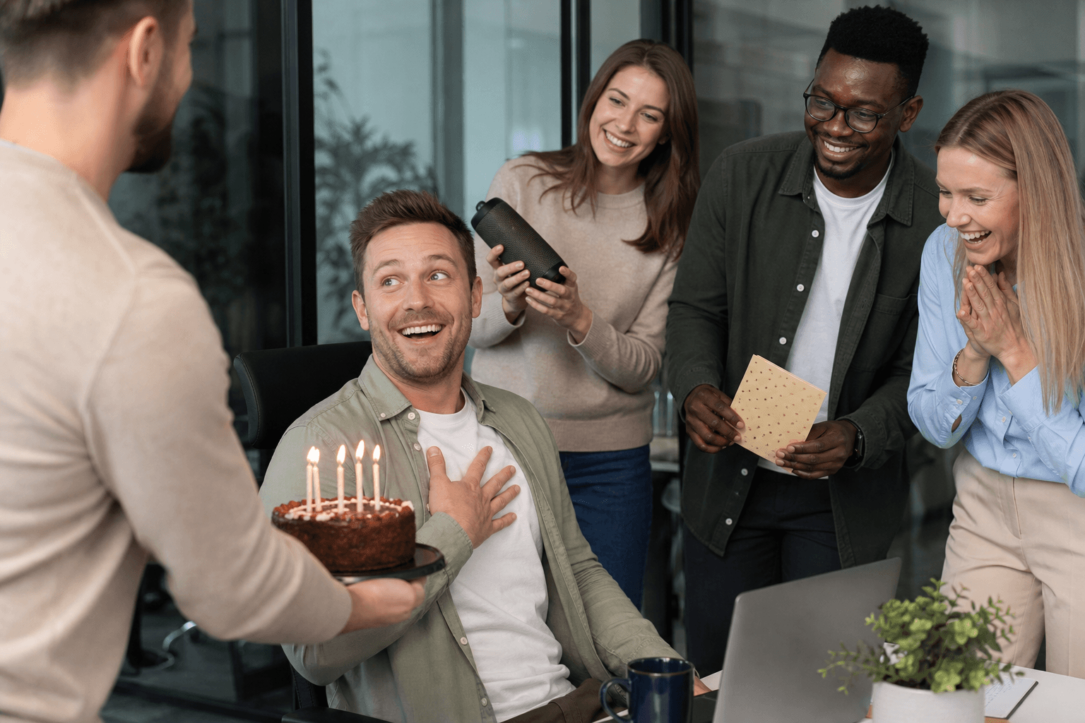 Kollegen überraschen einen Mann im Büro mit Kuchen, Karte und Lautsprecher zum Geburtstag